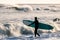 Surfer walking into ocean with board as waves crash