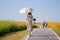 A surfer wearing a vintage dress carrying a sun umbrella traveling in the cosmos flower field to see the beauty of the colorful