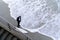 Surfer wearing wetsuit with surfboard watching ocean waves crash over rocks at St. Clair beach, Dunedin, New Zealand