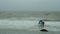 Surfer with windsurfing board approaching to the wavy water during bad stormy irish weather.