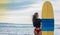 Surfer woman going surfing standing with blue-yellow surfboard on Waikiki Beach. Female bikini girl walking with surfboard living