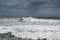 Surfers in in big waves at Alexandra Headland Beach under dark cloudy skies