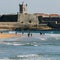 Surfers at Carcavelos beach, Lisbon Region, Portugal with historic fort in the