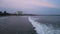 Surfers catch waves at dusk in crowded sea. Beginner surfers paddle out as sunset colors sky. Aerial view shows