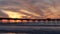 Surfers surfing by pier. Ocean water waves, people and sky at sunset. California