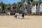 Surfers walking across the sandy beach with surf boards surrounded by swing sets, hotels and office buildings