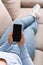 Surfing in internet. Woman in jeans lies on sofa and holds phone with blank screen