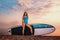 Surfing and sport. A young slender tanned woman poses with a sup board. Sunset in the background. Copy space