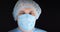 The surgeon looks at the camera in a blue uniform, surgical gown, mask and cap. On a black isolated background, a male