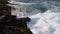 Surging sea waves crash against rocky shore. Coastal scenery with foamy tides, marine power display. Cinematic view for