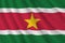 Suriname flag with big folds waving close up under the studio light indoors. The official symbols and colors in banner