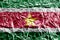 Suriname flag depicted in paint colors on shiny crumpled aluminium foil closeup. Textured banner on rough background