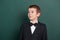 Surpised school boy portrait near green blank chalkboard background, dressed in classic black suit, one pupil, education concept