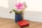 Surprise gift and flowers. Pink orchid and gift box indoors on the floor, background light solar wall, copy space.