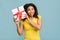 Surprise gift. Overjoyed black woman holding present, shaking whapped box over blue studio background.