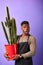 Surprised African farmer in apron standing with a big cactus  on purple