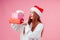 Surprised amazed redhaired ginger woman in knitted sweater and red santas claus hat holding many gift boxes, cute white