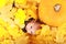 Surprised baby boy lying by pumpkin covered by maple leaves