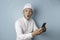 Surprised Balinese man wearing udeng or traditional headband and white shirt holding his smartphone, isolated by blue background