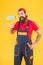 surprised bearded male painter worker in boiler suit uniform using paint roller tool for painting wall into yellow color