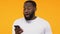 Surprised black man looking at smartphone, mobile app update, yellow background