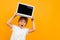 Surprised boy holds a laptop on his head with a mockup on a yellow background with copy space