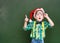 surprised boy in red christmas hat near a green chalkboard showing finger up