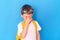 Surprised boy with a yellow briefcase rubs his eyes against a blue background