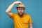 Surprised Caucasian man in round glasses clings to his hat, as if greeting someone, on a blue background.