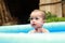 Surprised cute baby boy in blue inflating pool