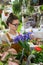 Surprised florist woman surrounded by houseplants, holding at a bouquet of irises flowers. Indoor garden