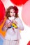 Surprised frightened girl in the hat of a large bow on a background of bright rubber air balls