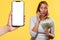 A surprised girl holds a fan of dollars and talks on the phone. On the left is a smartphone with a white screen. Mock up. Yellow