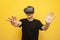 Surprised guy with VR glasses touches virtual space on a yellow background, using modern virtual reality gadgets
