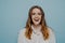 Surprised happy brunette woman of young age against blue wall