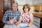 Surprised husband and wife looking at bills with cash money in hands, domestic kitchen