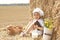 Surprised kid is holding a bagel and coarse bread in hand while sitting in a field by a stack of straw.