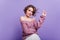 Surprised lady in stylish pink shoes standing on one leg and pointing finger. Indoor photo of cute curly girl in sweater
