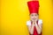 Surprised little girl in a red chef`s suit with hands on cheeks on yellow background with copy space