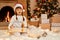 Surprised little girl wearing white sweater and santa claus hat, posing with dog in festive room with fireplace and Xmas tree,