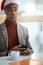 Surprised look of young afro-american in the office, texting on cell phone, wearing santa hat with cup of coffee in front of him