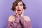 Surprised lovely girl with beautiful eyes posing in studio with purple interior. Indoor photo of curly brunette young