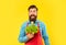 Surprised man in apron holding fresh lettuce and juice bottle yellow background, juice barkeeper