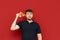 Surprised man with beard stands on red background with piece of pizza in hand, looks into camera with shocked face. Hungry guy