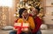 Surprised millennial african american woman looks at husband, he gives gift with red ribbon in living room