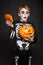Surprised red hair child in Halloween costume holding a orange pumpkin. Skeleton