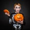 Surprised red hair kid in Halloween costume holding a orange pumpkin. Skeleton