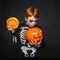 Surprised red haired boy in skeleton costume holding a orange pumpkin. Halloween.