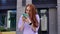 Surprised redhead girl reading good news on phone outdoors background of city street.