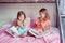 Surprised scared Caucasian sisters girls reading books in bedroom. Home schooling children siblings learned saw unexpected in a